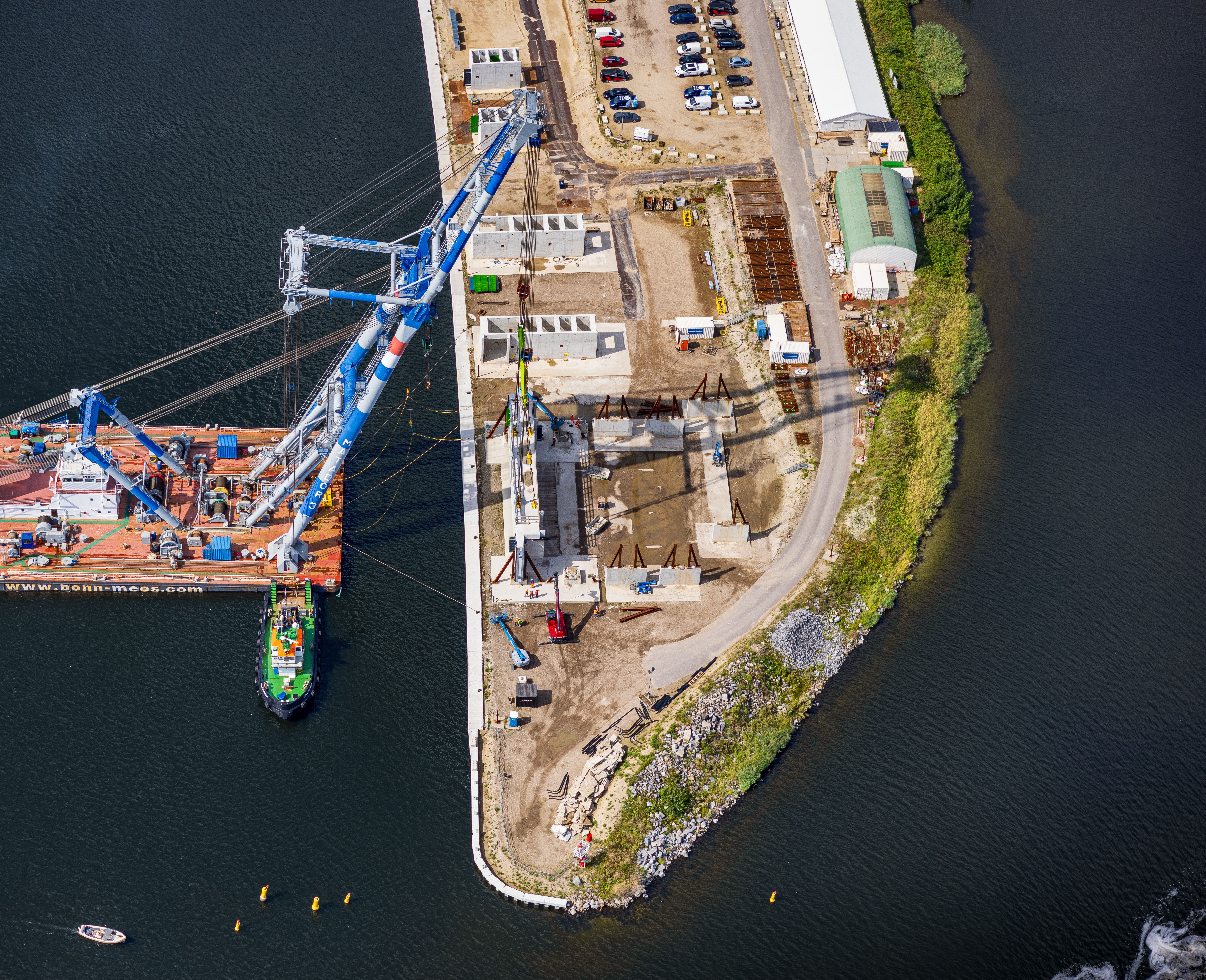 Luchtfoto van bouwplaats aan water met grote kraan op ponton, schepen en constructie-elementen voor zoutdam IJmuiden.