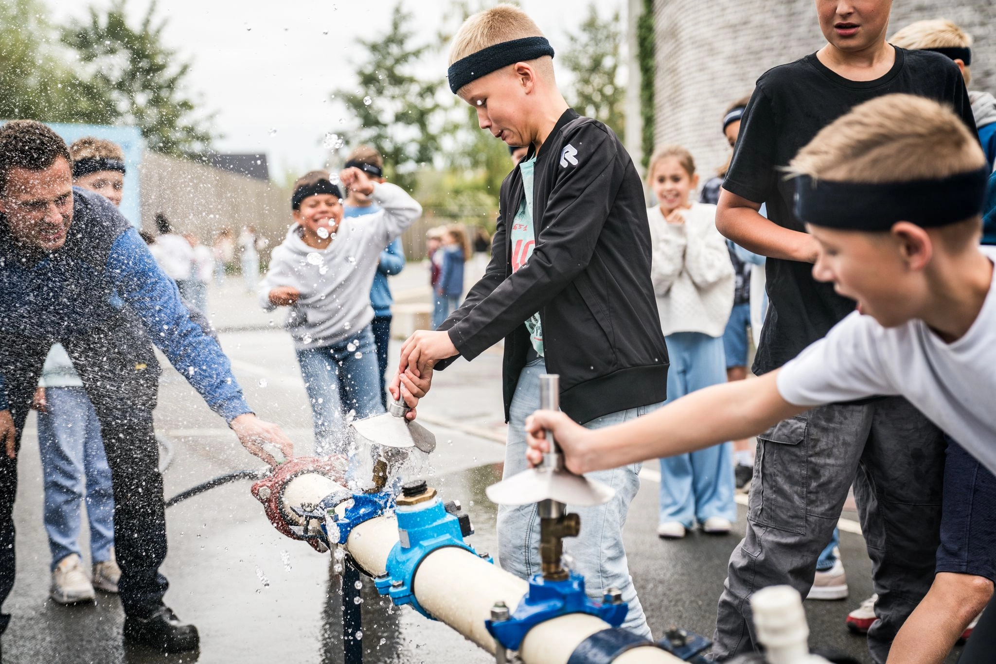 Kinderen bedienen waterkranen buiten, waarbij water opspat als onderdeel van een leeractiviteit over water.