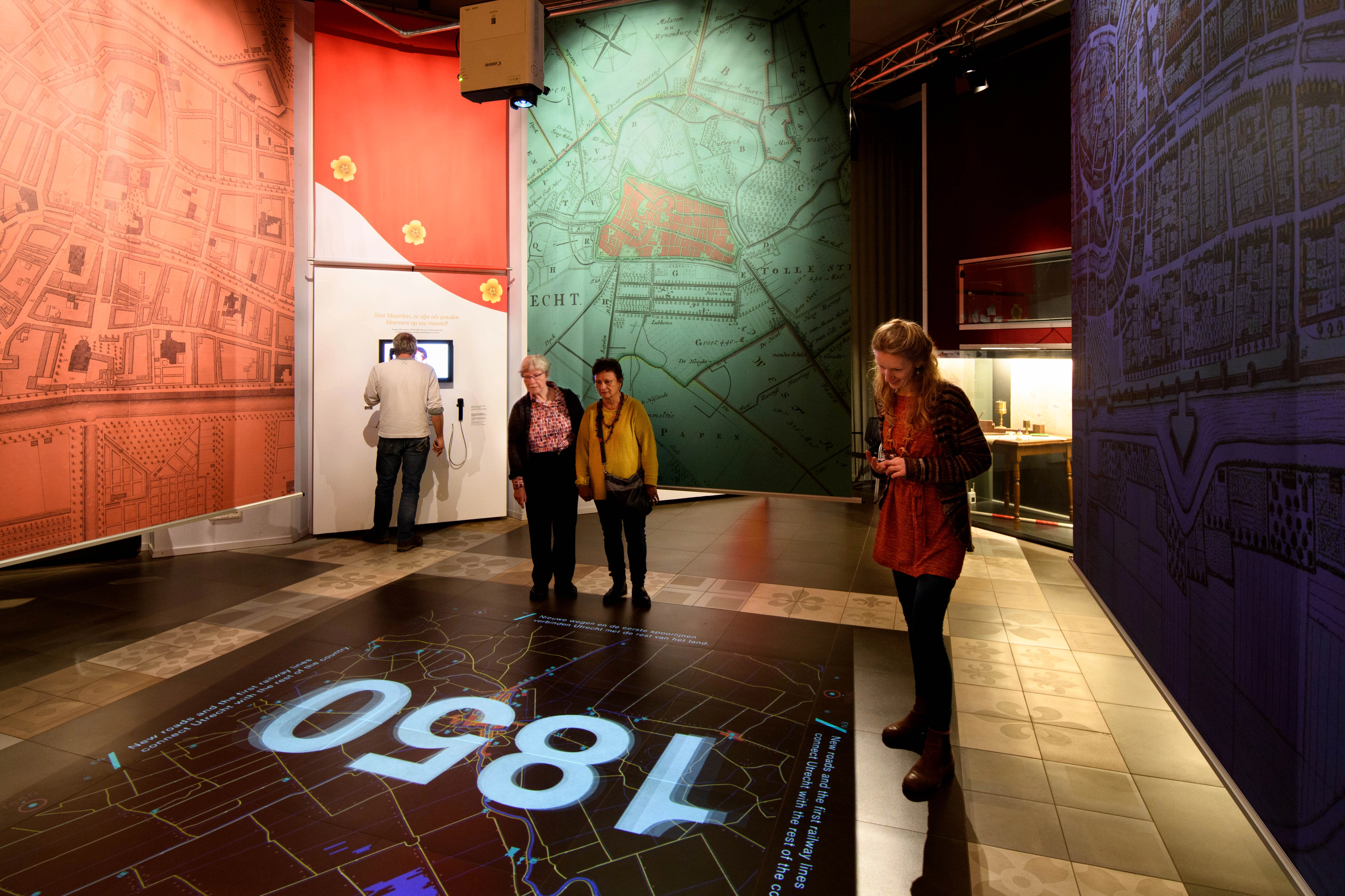 Ruimte met grote historische stadskaarten op wanden en vloerprojectie ‘1850’, bezoekers verkennen.