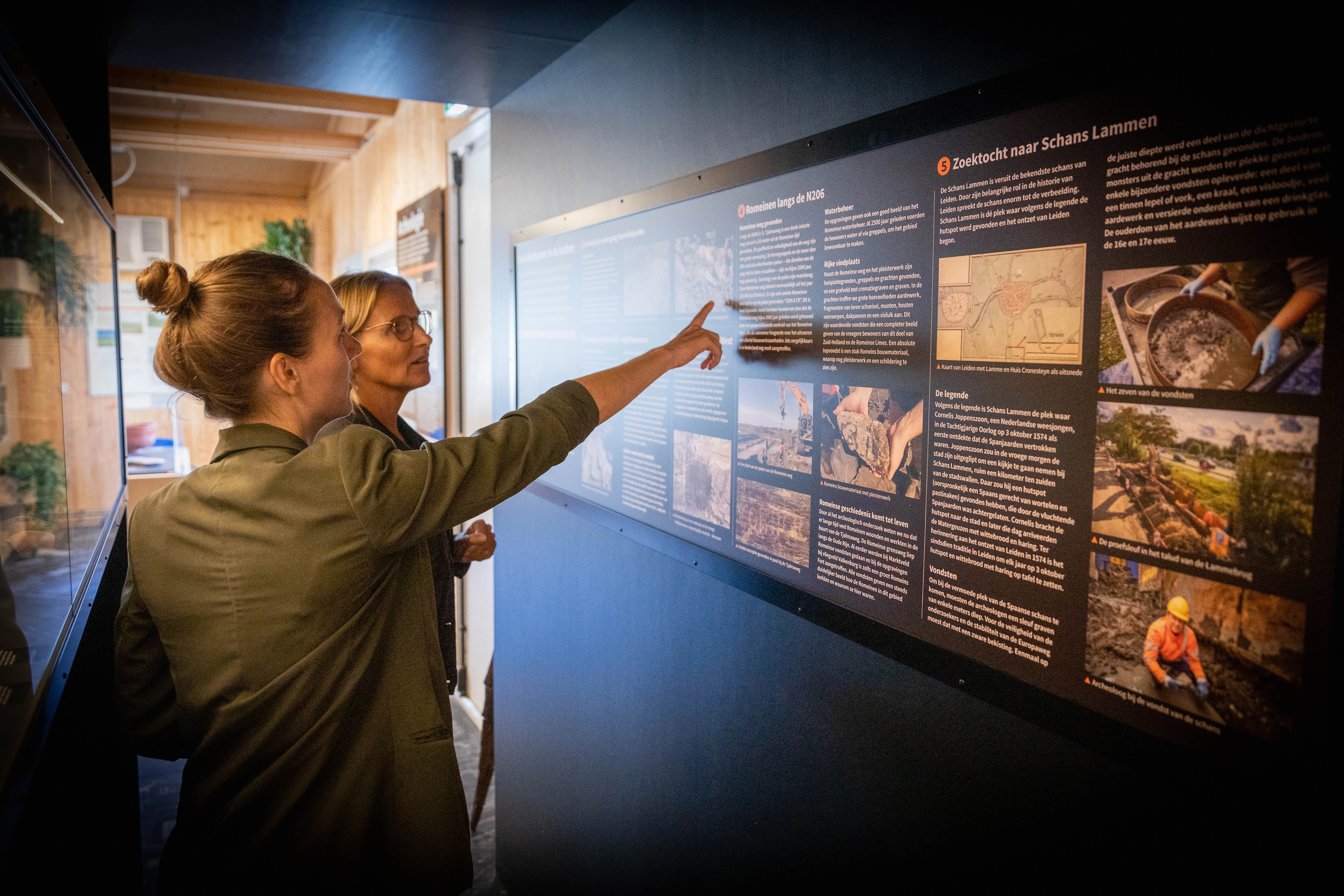 Twee vrouwen kijken naar een informatiebord met tekst en afbeeldingen in het informatiecentrum van de RijnlandRoute